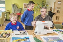 Artist Cefyn Burgess with school children from Ysgol Hendre working on the Patagonia project with residents at Bryn Seiont, Caernarfon. Artist Cefyn Burgess explains the sewing machine to Ian owenm 10 and Kieran Roberts, 10.